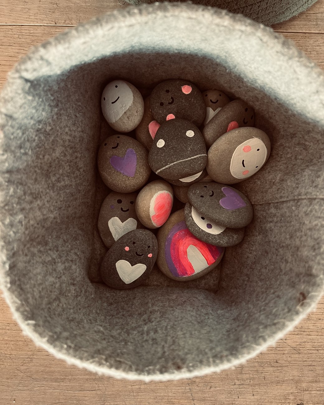 A soft felt basket filled with smooth pebbles, each painted with a smiling face, a heart or a rainbow